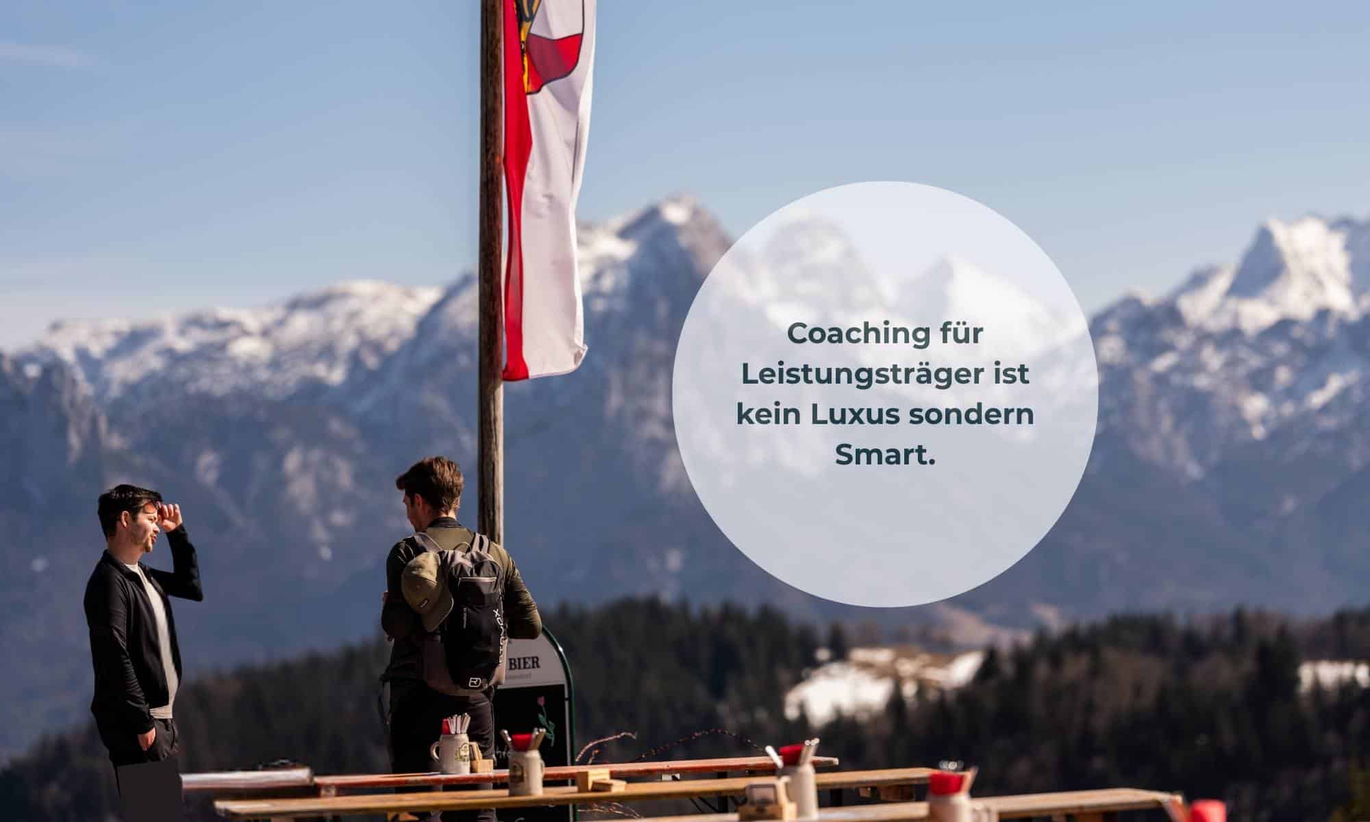 2 junge Männer auf einer Almhütte am reden vor dem Bergpanorama